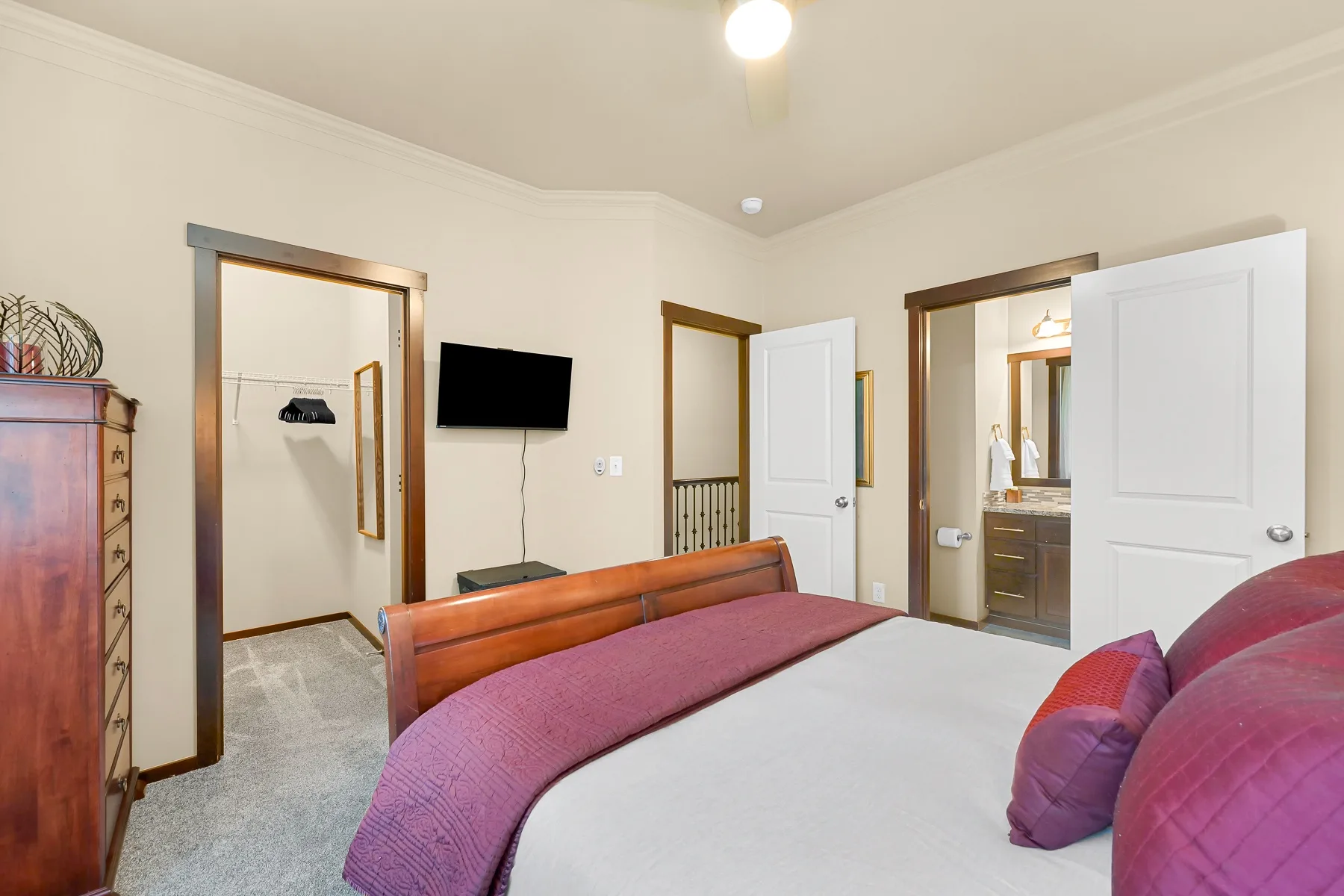A bedroom with a bed, a wall-mounted television, and open doors to adjoining rooms.