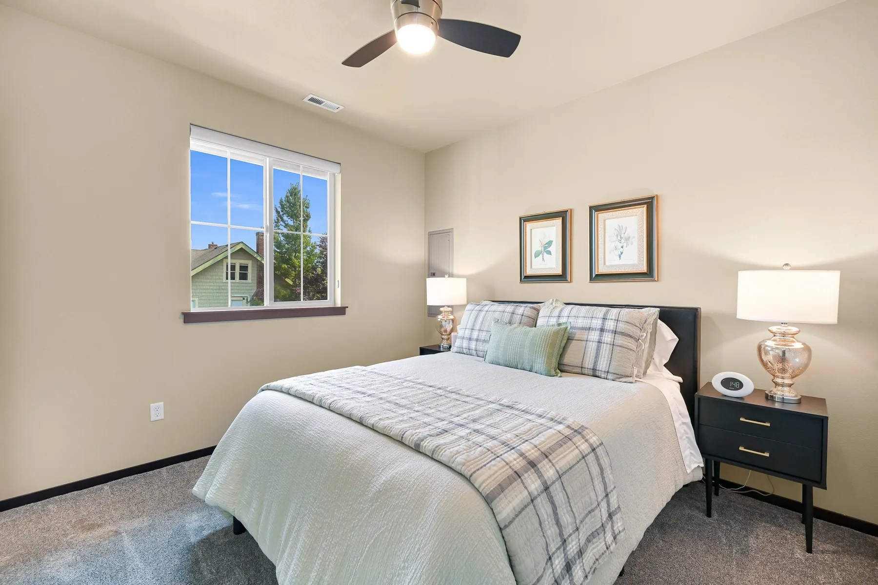 A bedroom with a bed, bedside tables, and a window overlooking neighboring houses.
