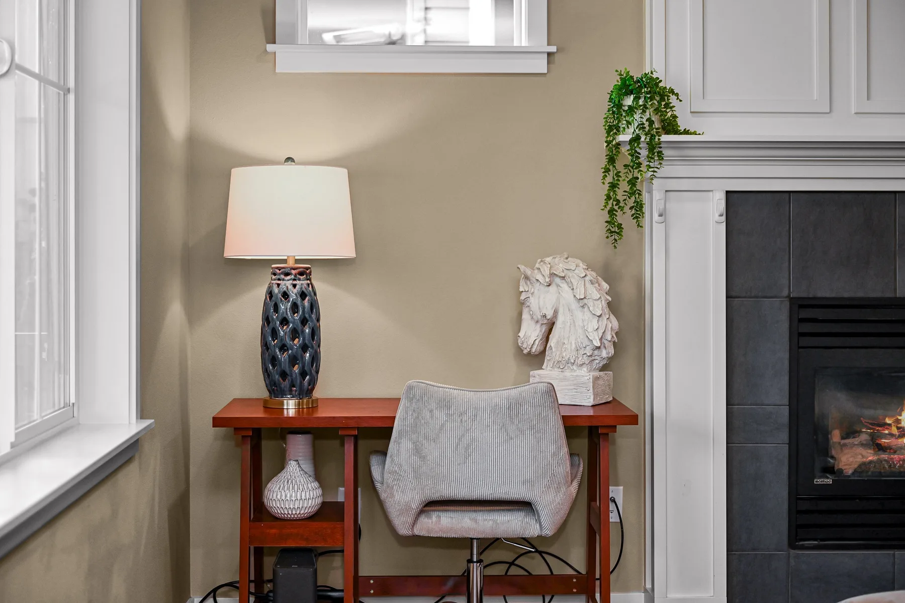 A desk and chair sit beside a fireplace in a neutral-toned room.