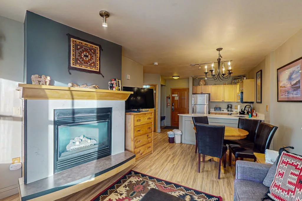 A living room opens onto a kitchen and dining area, with a fireplace and table.
