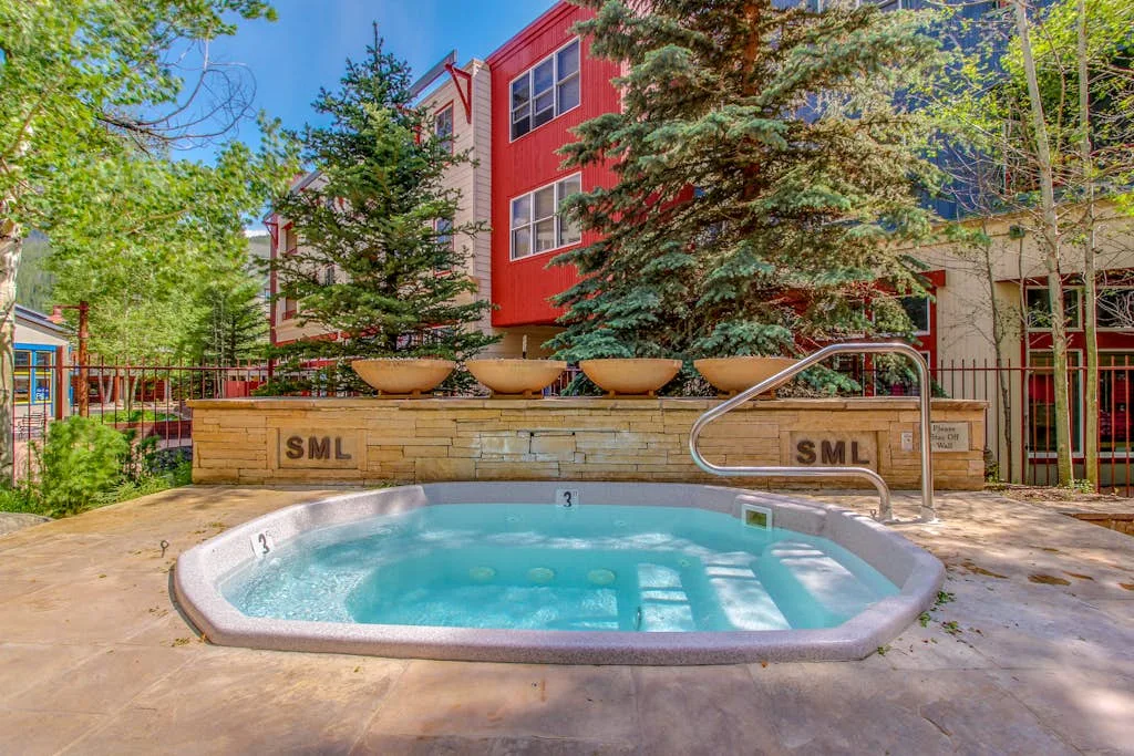 An outdoor hot tub sits on a paved patio beside a landscaped building.