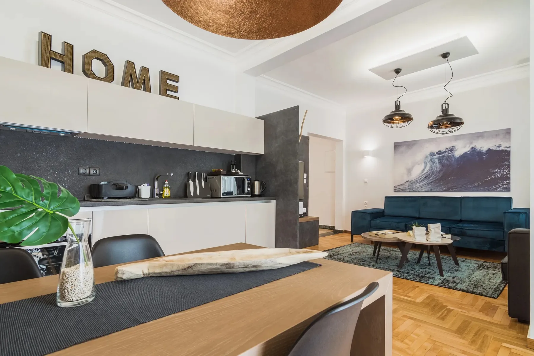 An open-plan kitchen and living area with a dining table and blue seating.