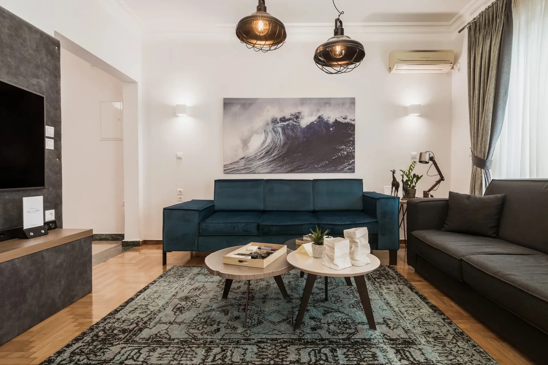 A living room with teal seating, a rug, and a wall-mounted television.