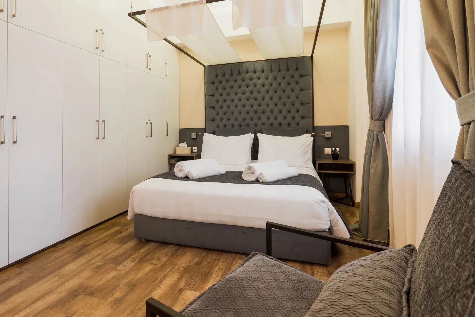 A bedroom with a neatly made bed and a seating area beside the window.