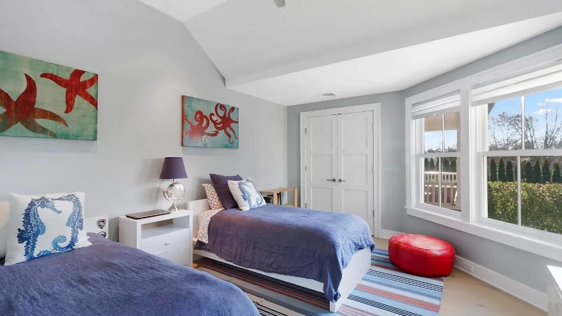 A bright bedroom with two beds, large windows, and colorful wall art.