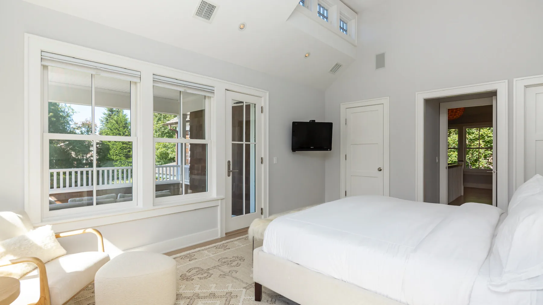 A bright bedroom with a bed, windows, and a wall-mounted television.