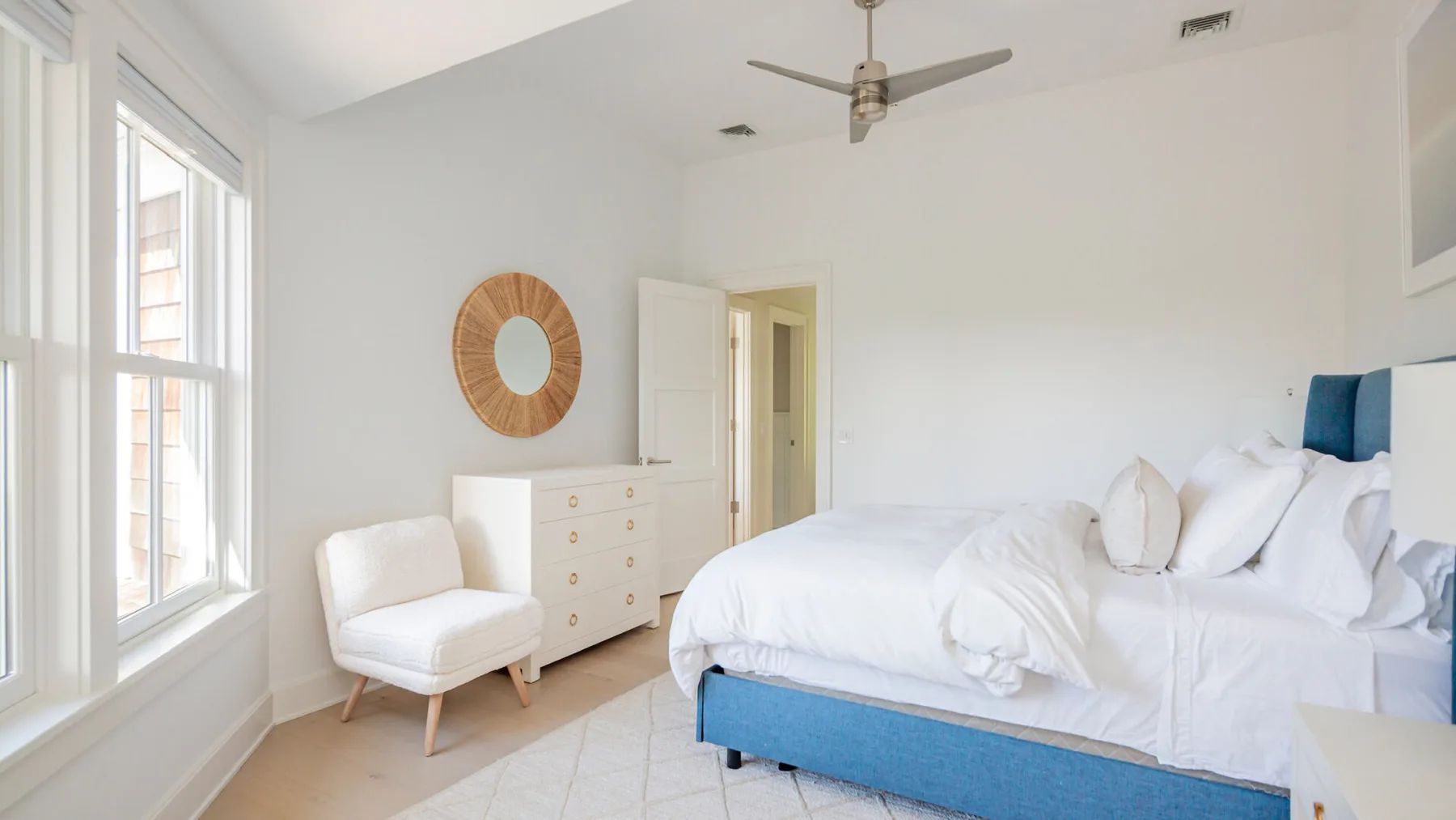 A bright bedroom with a white bed and large windows.