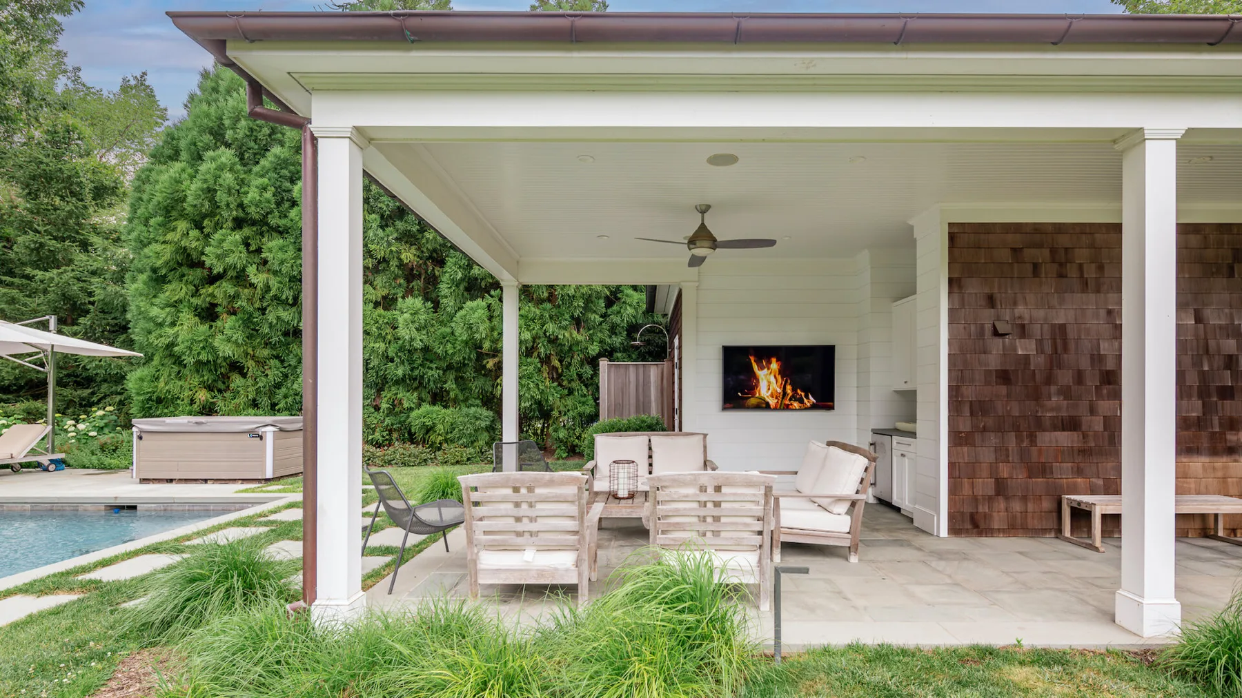 A covered outdoor patio has seating arranged around a table beside a pool.