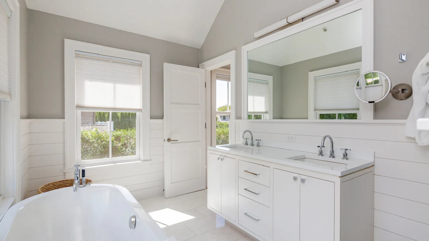 A bright bathroom with a bathtub, white vanity, and large mirror.