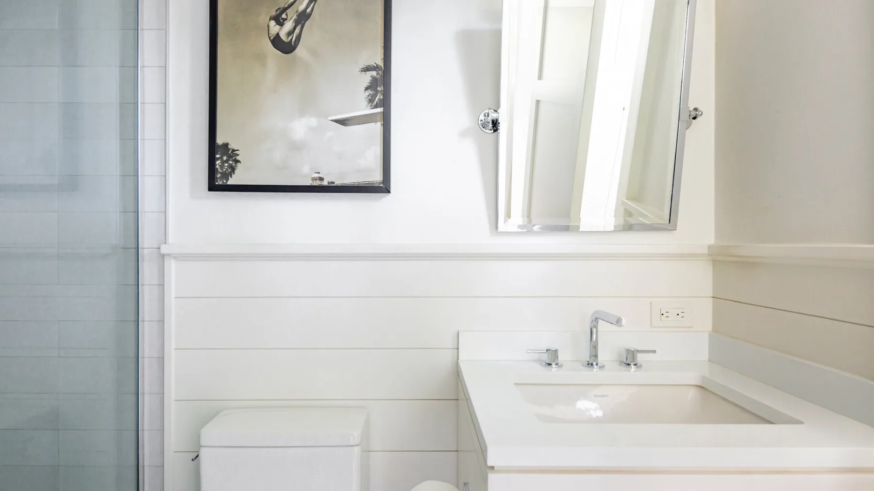 A bright bathroom with a sink, mirror, and glass shower.