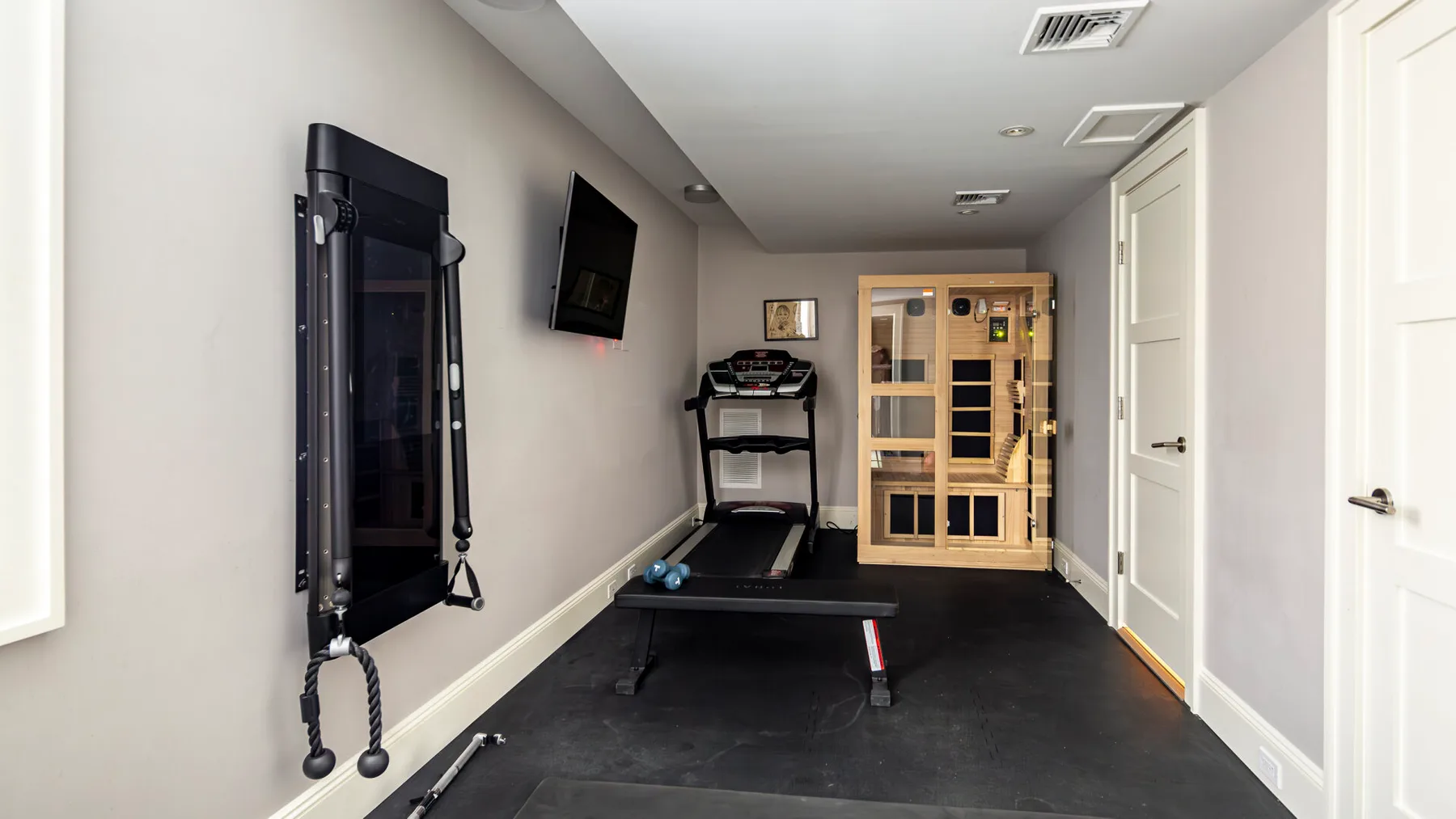A home gym with exercise equipment and a glass-fronted sauna.