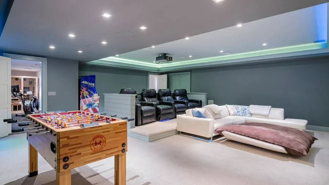 A recreation room with a foosball table, reclining seats, and a sectional sofa.