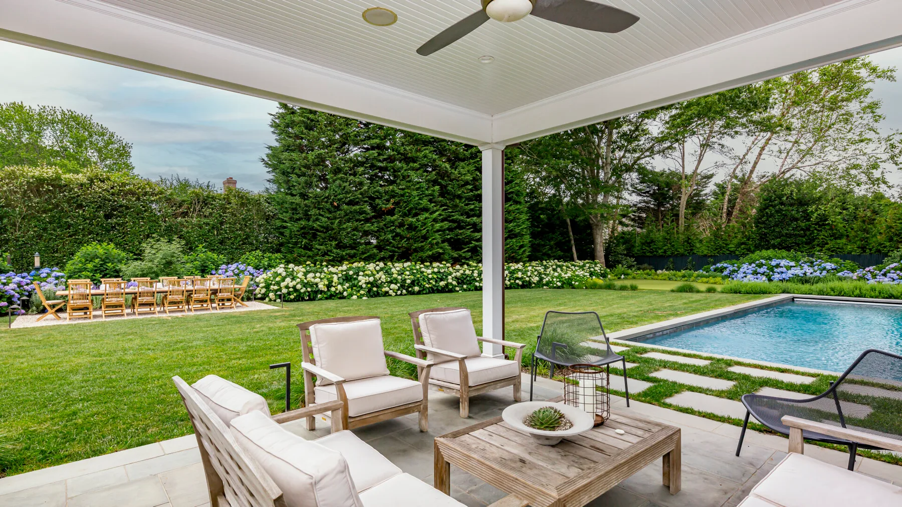 A covered patio overlooks a garden and swimming pool, with outdoor seating.