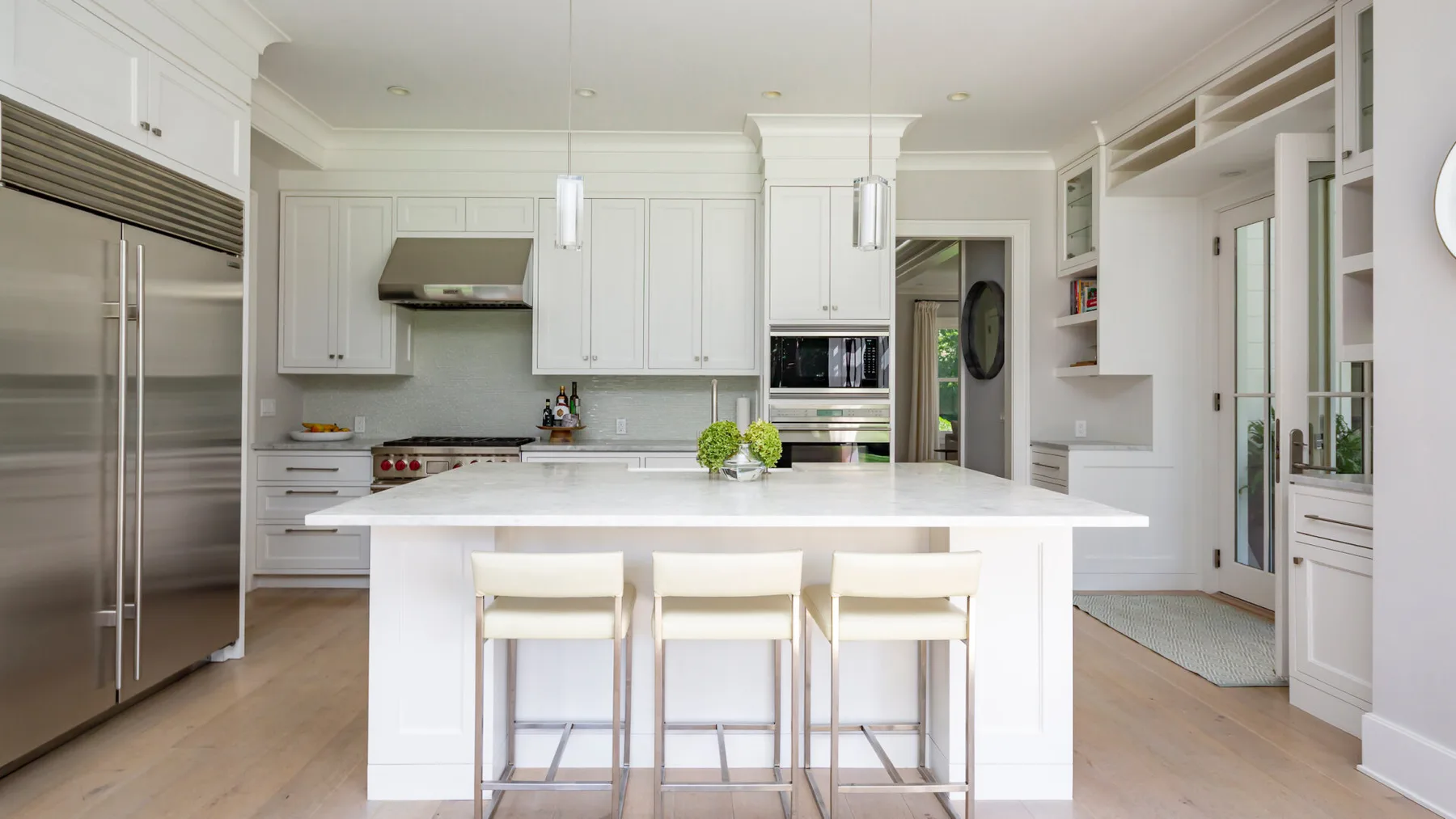 A bright white kitchen with a central island and three stools.