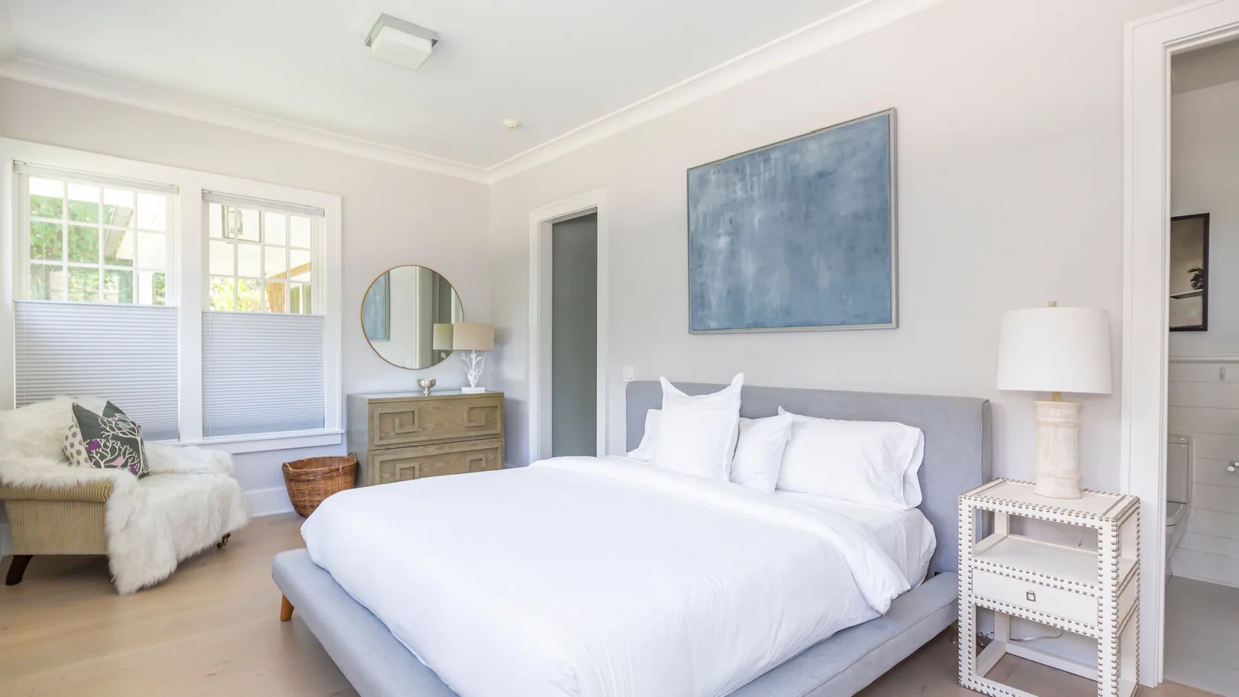 A bright bedroom with a large bed, a dresser, and windows.