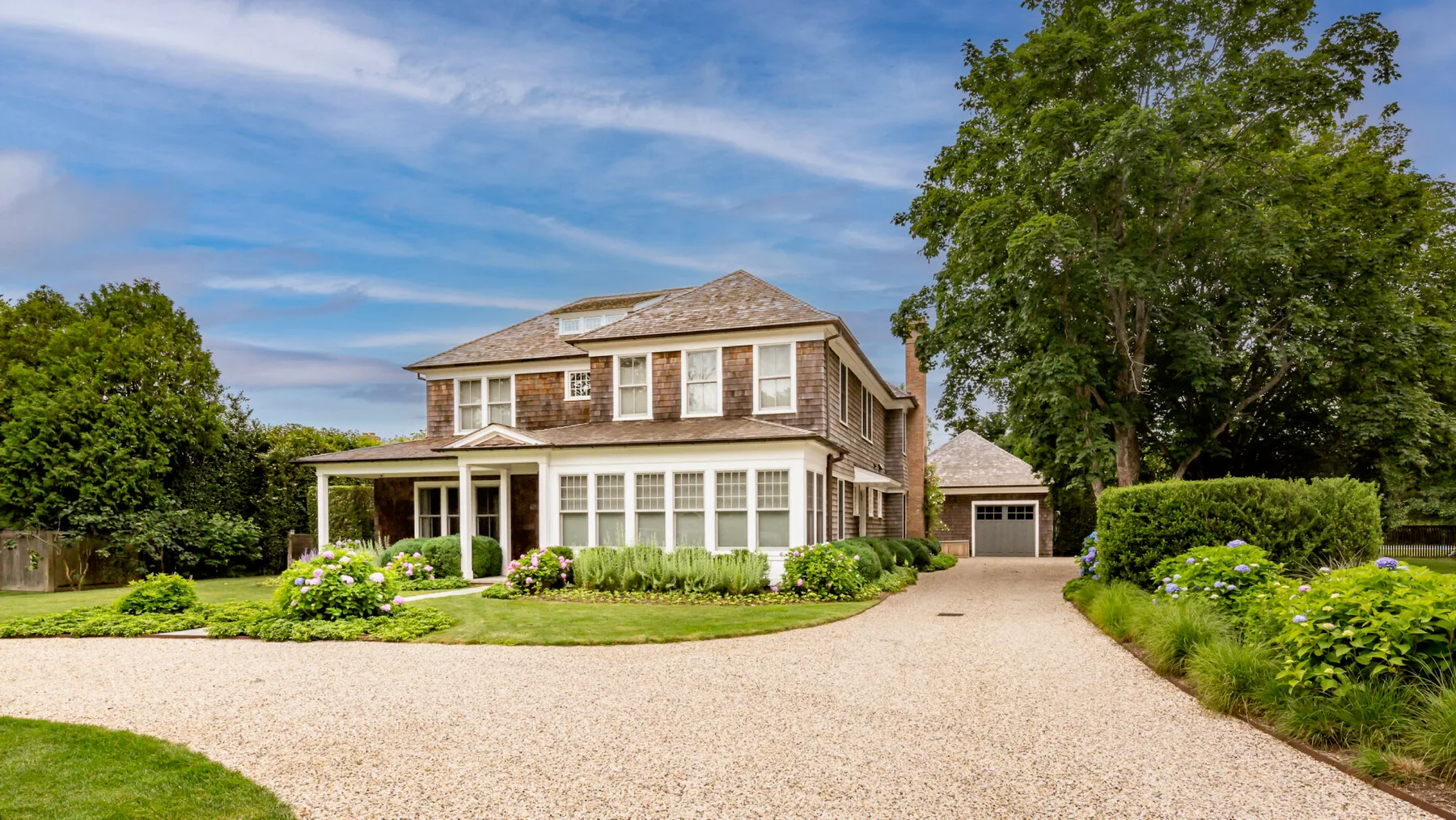 A large brick house stands beside a gravel driveway and landscaped garden.