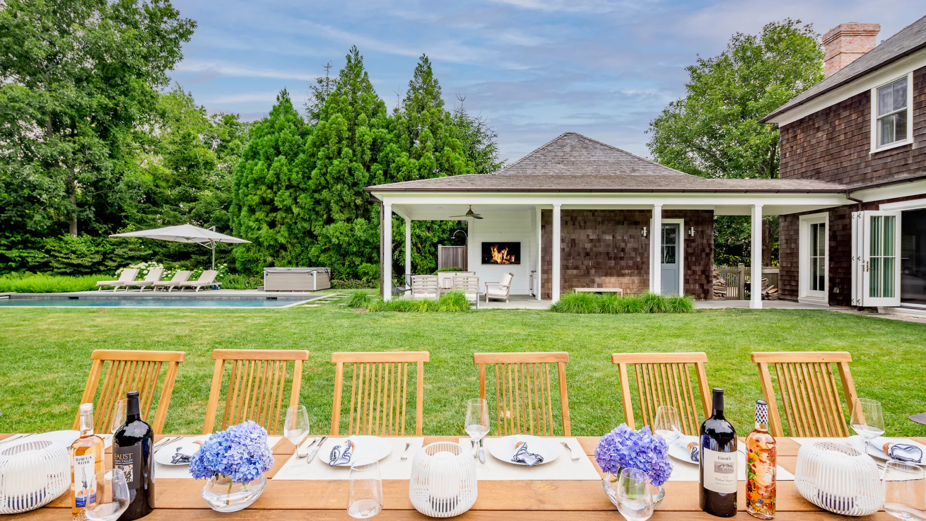 A lawn-side outdoor dining table faces a covered patio and swimming pool.