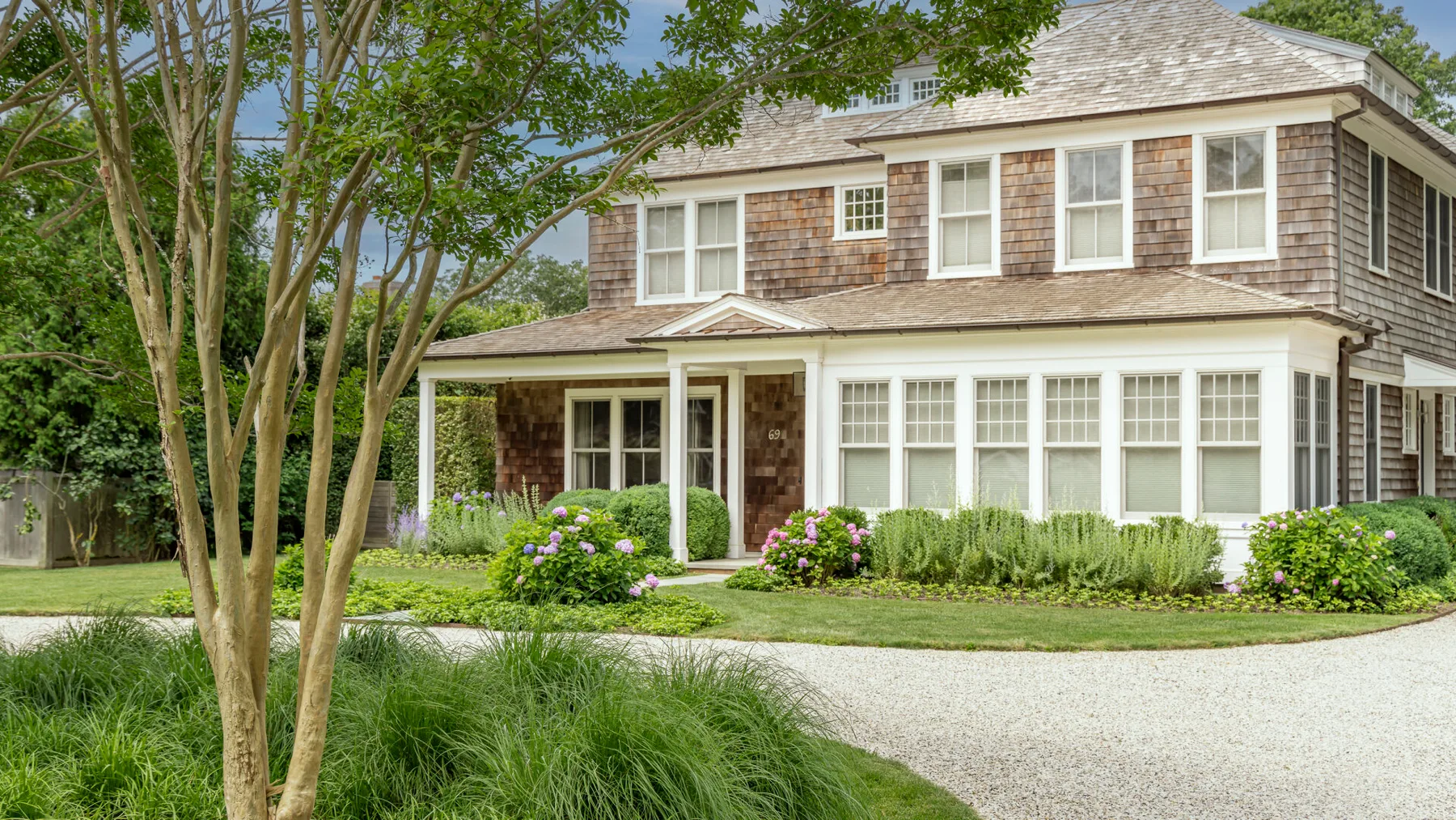 A two-story house with a covered porch, garden beds, and a curved gravel driveway.