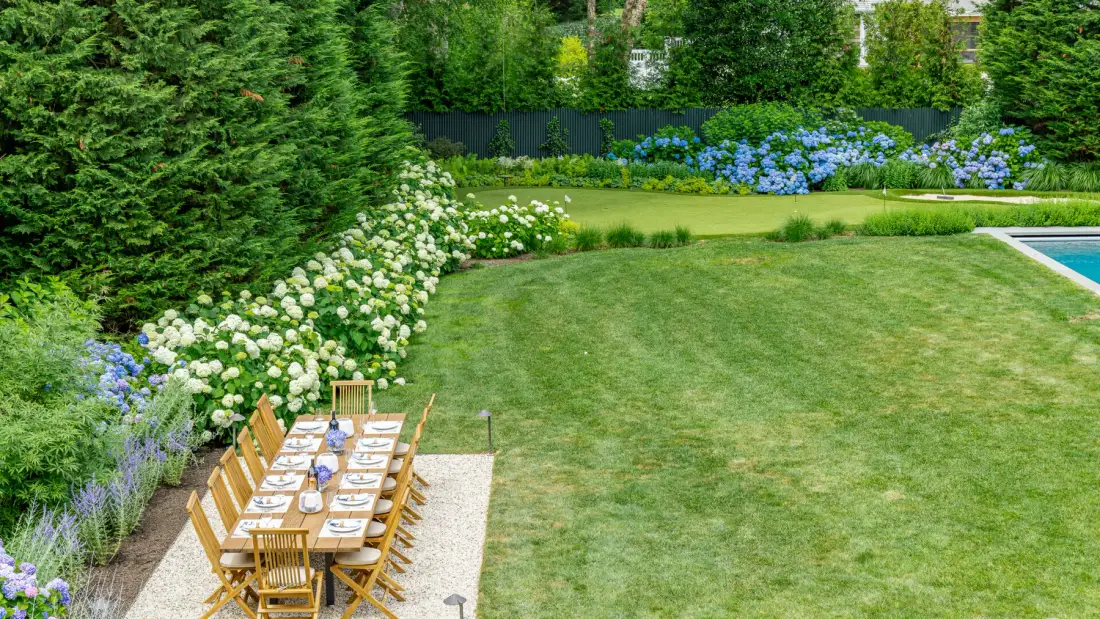 A garden lawn beside an outdoor dining area, with flowering shrubs along the edge.
