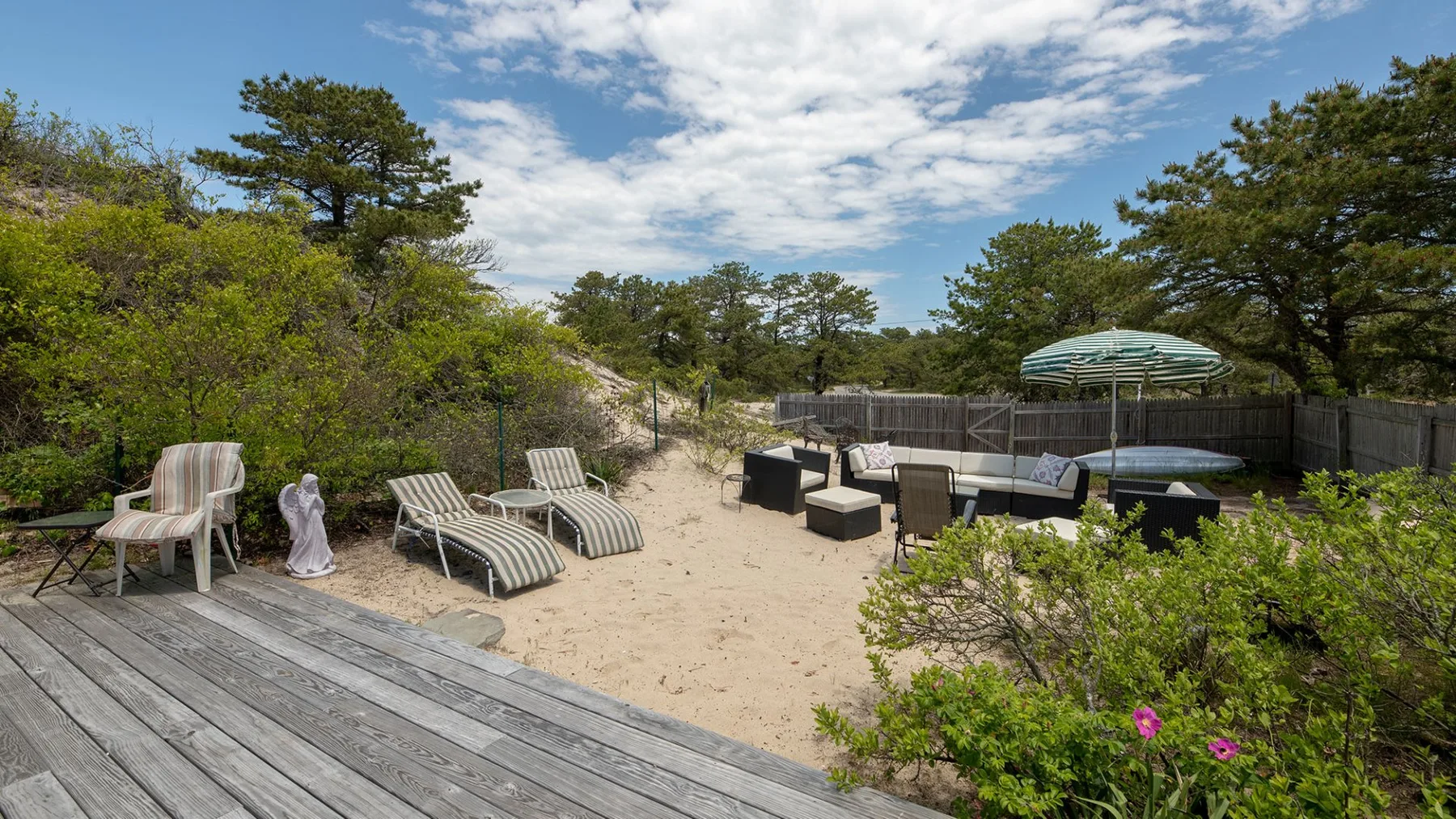 Un patio exterior de arena con asientos, una terraza de madera y árboles alrededor.