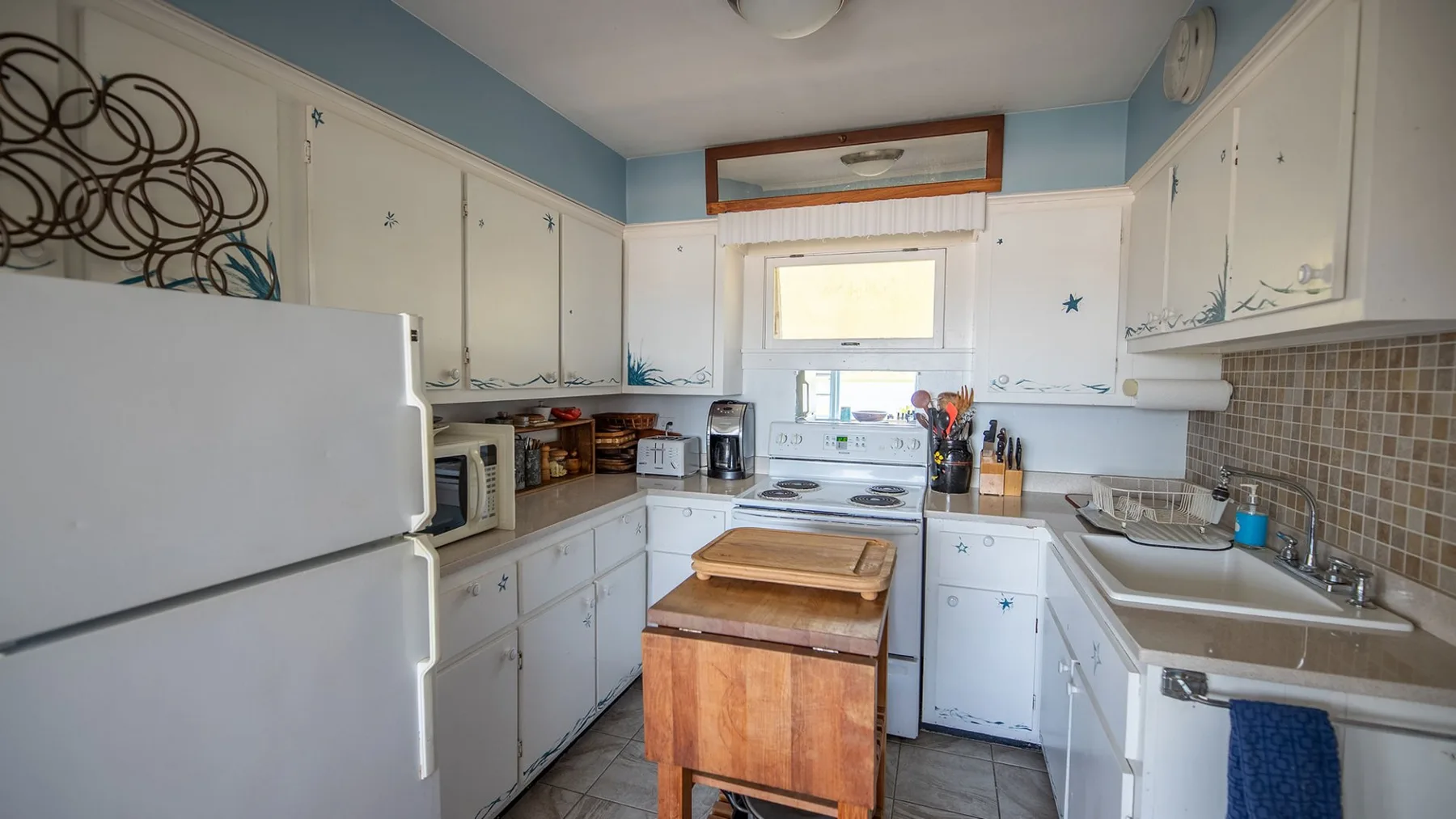 Una cocina compacta con gabinetes blancos, una isla central y un fregadero.