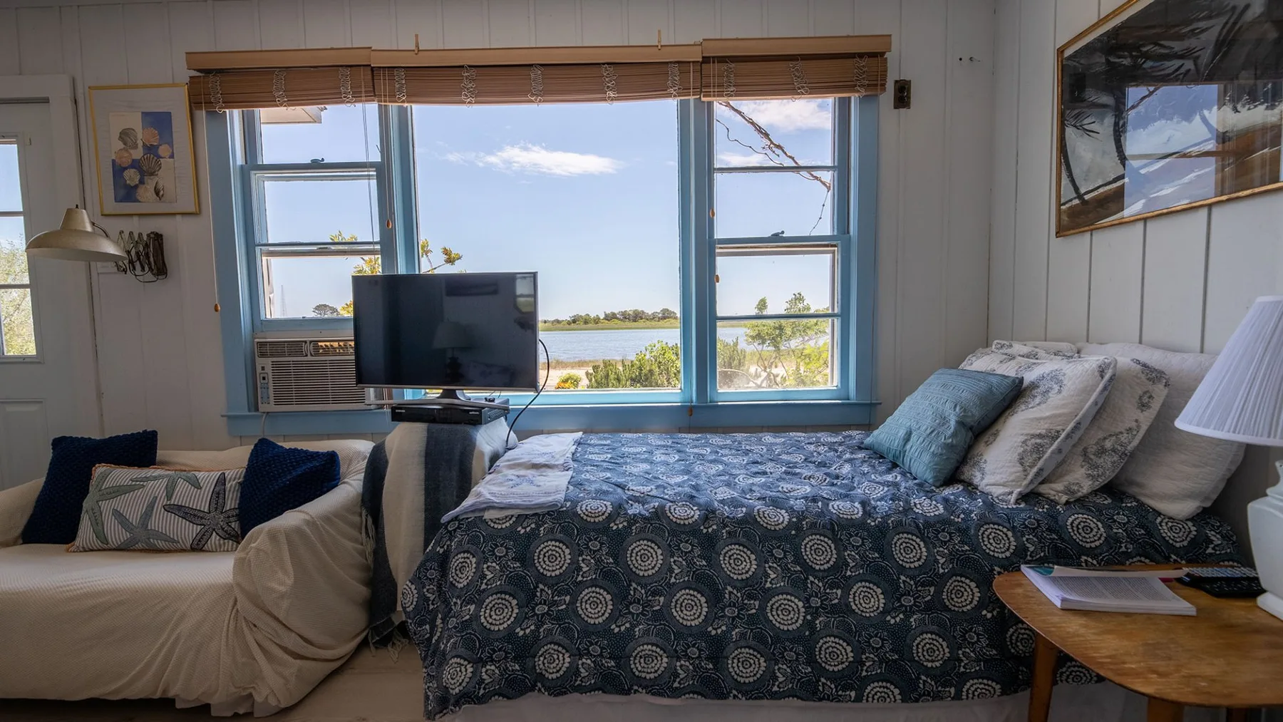 Un dormitorio con una cama estampada y una ventana amplia con vista al agua.