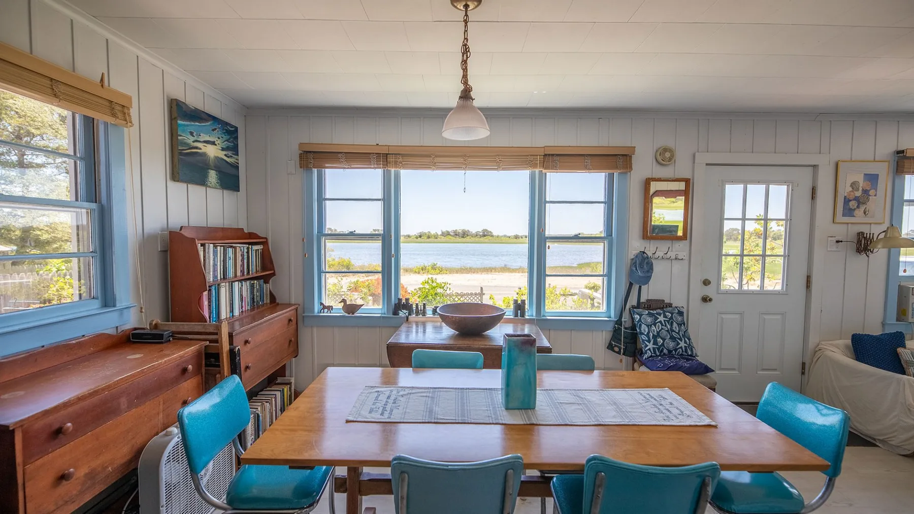 Un comedor con una mesa de madera y grandes ventanas con vistas al agua.
