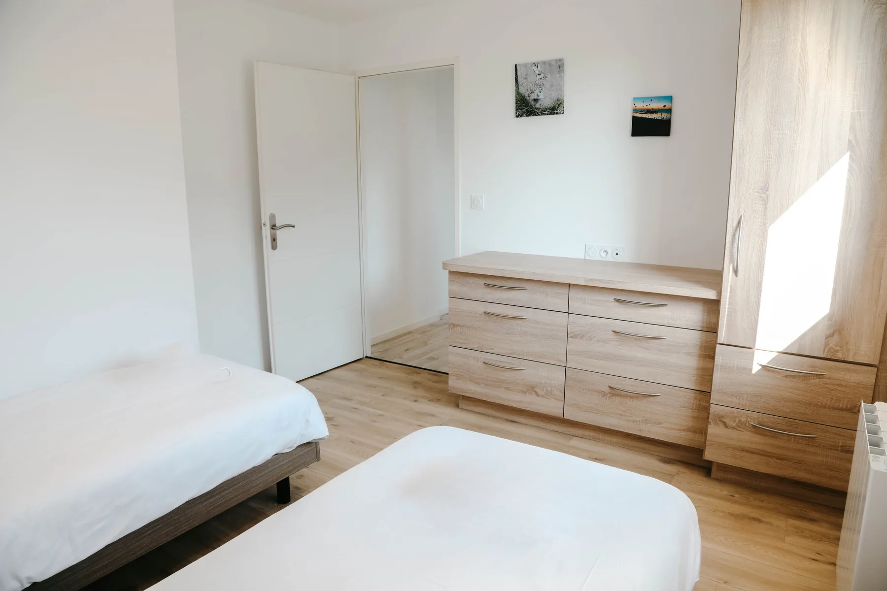 A bright bedroom with two beds and a wooden dresser.