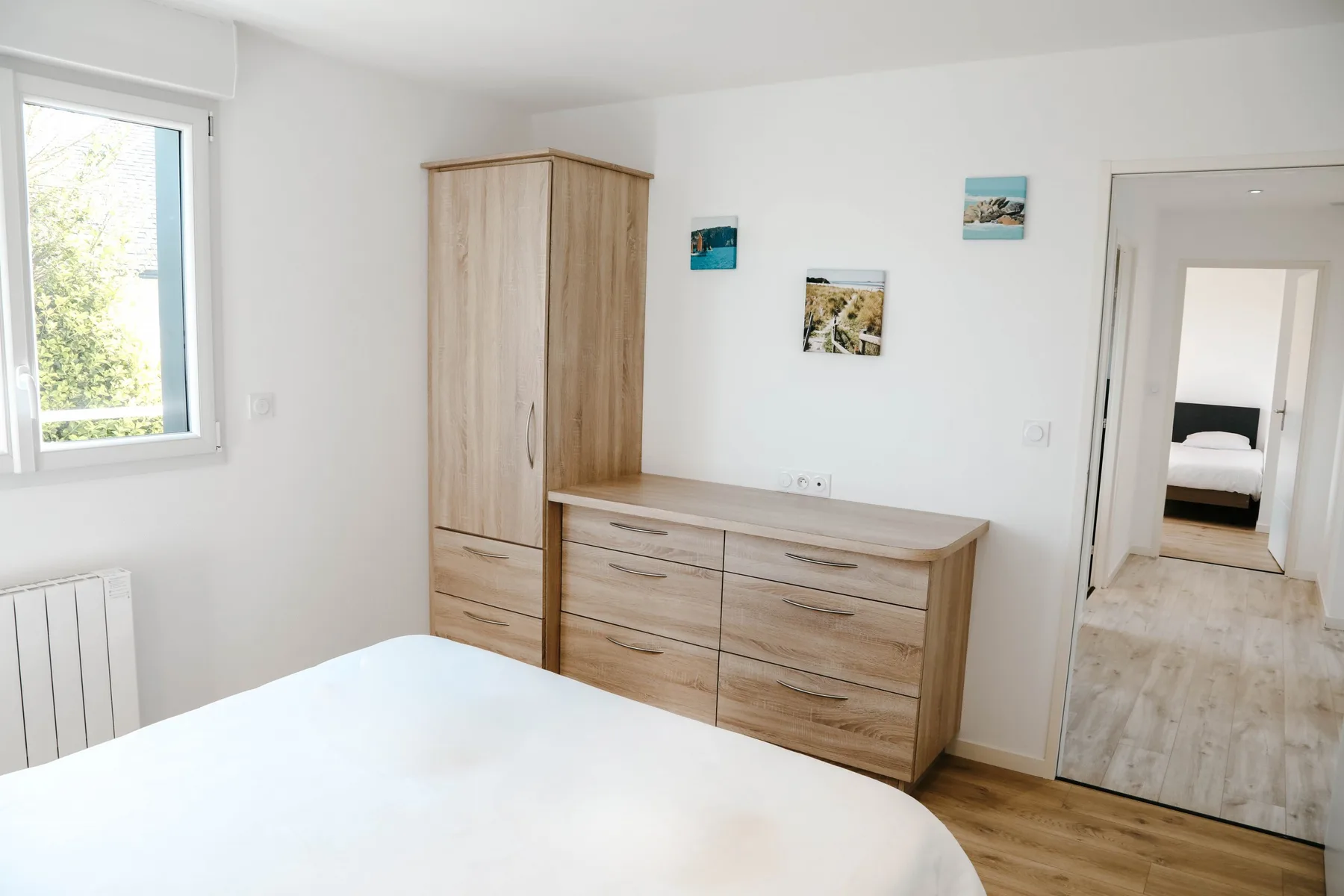 A bright bedroom with wooden storage furniture and a bed.