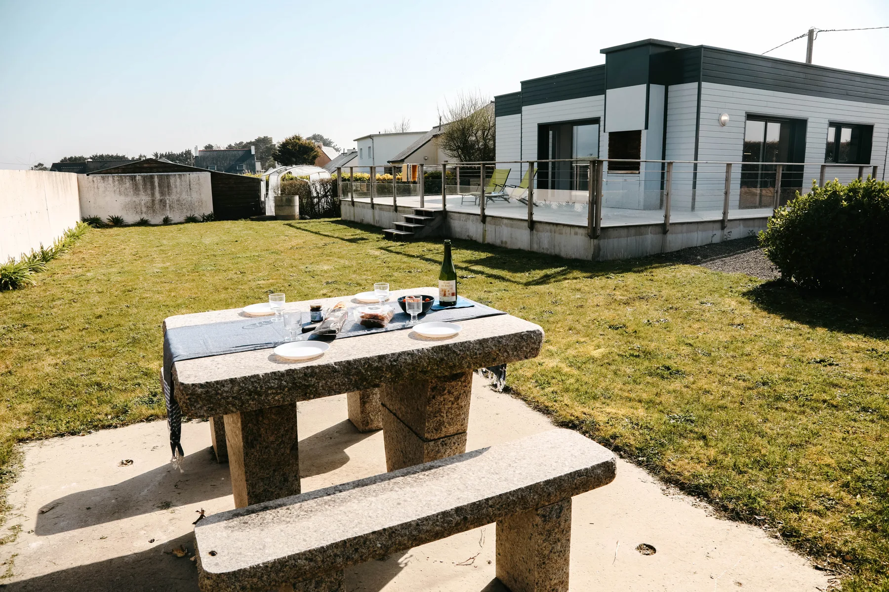 A picnic table set for dining sits on a patio beside a modern house.