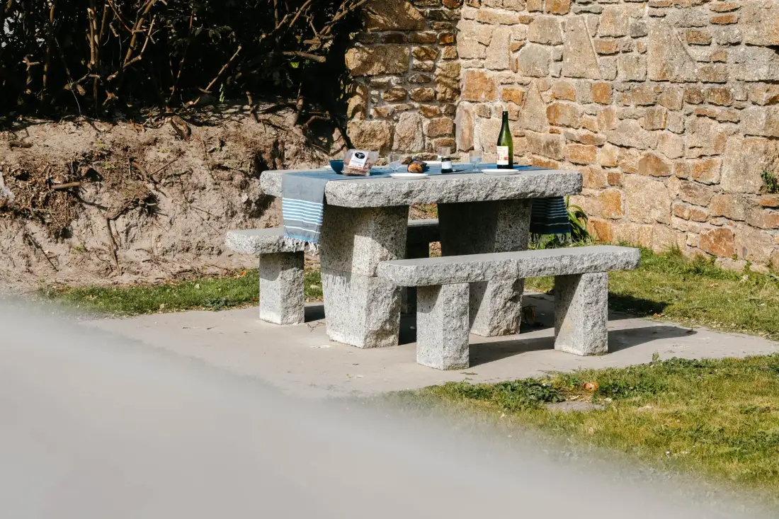 An outdoor stone picnic table and benches stand beside a stone wall.