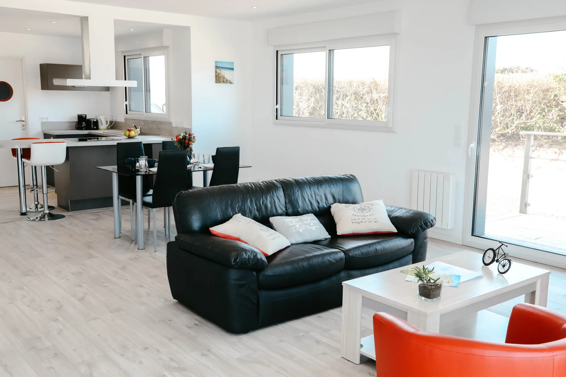 A bright open-plan living area with seating beside a dining table and kitchen.