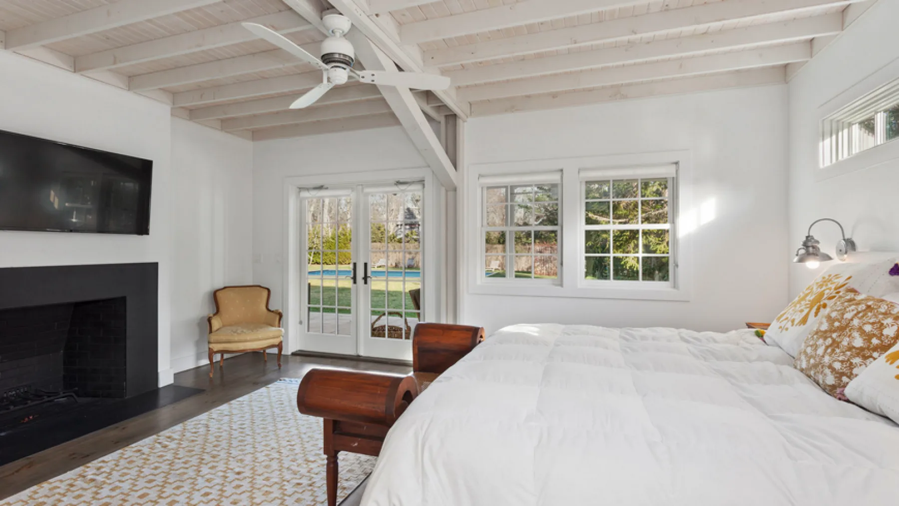 A bright bedroom with a large bed, a fireplace, and windows overlooking greenery.