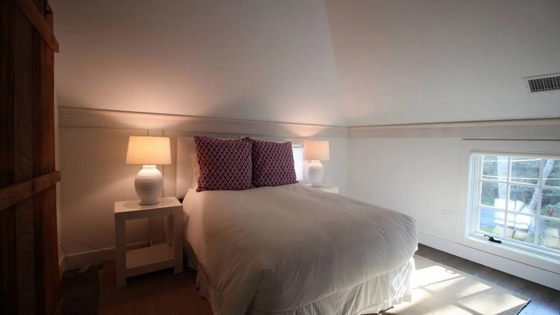 A bedroom with a bed, bedside tables, and a window.