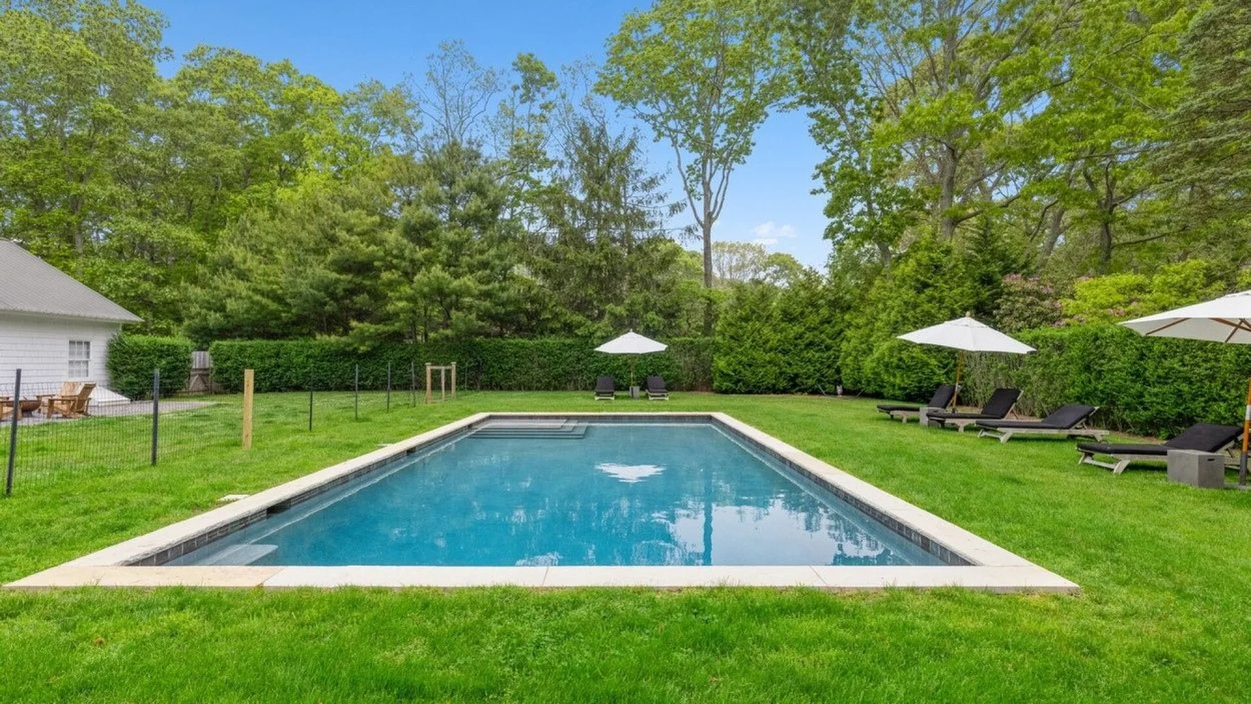 An outdoor swimming pool sits in a grassy yard surrounded by trees.
