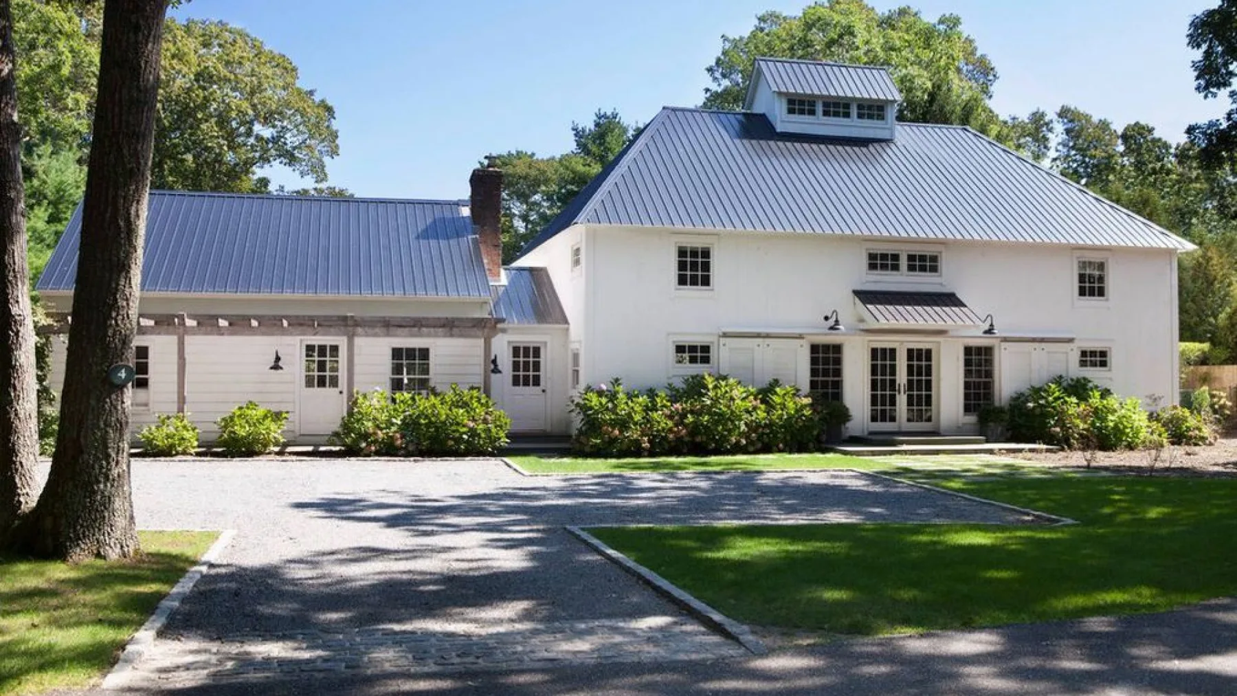 A large white building with a metal roof stands beside a paved driveway and green lawn.