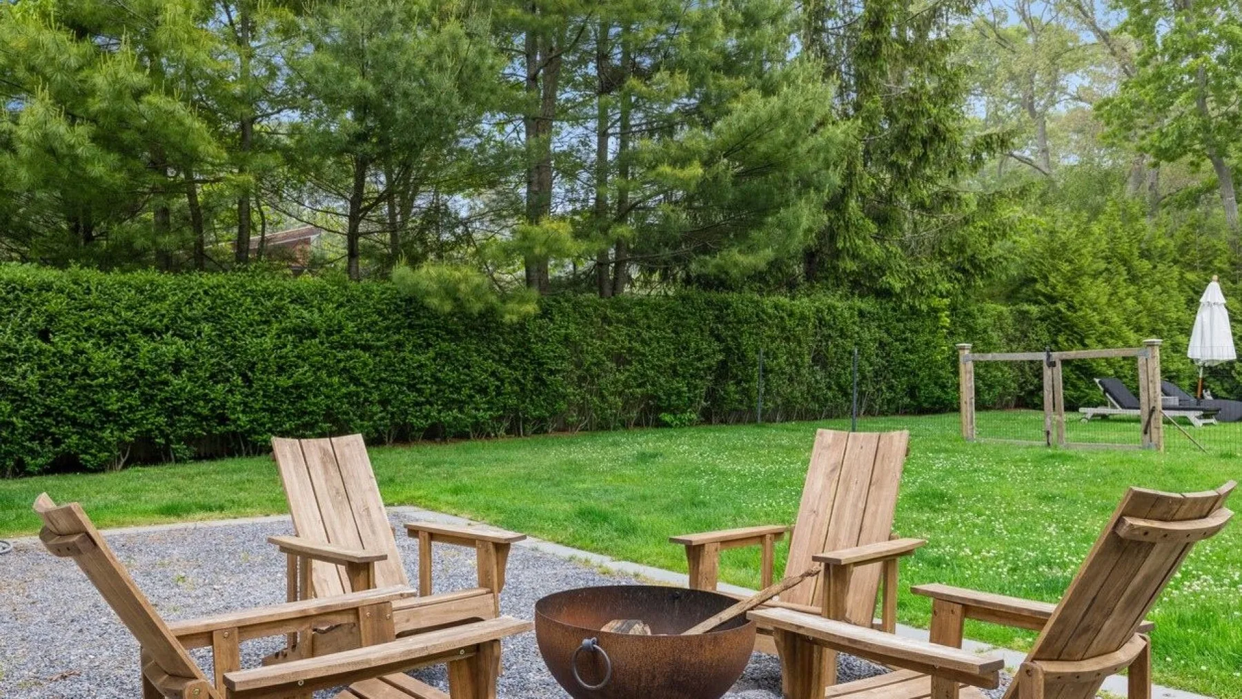 Asientos de madera al aire libre rodean un brasero junto a un jardín con césped.