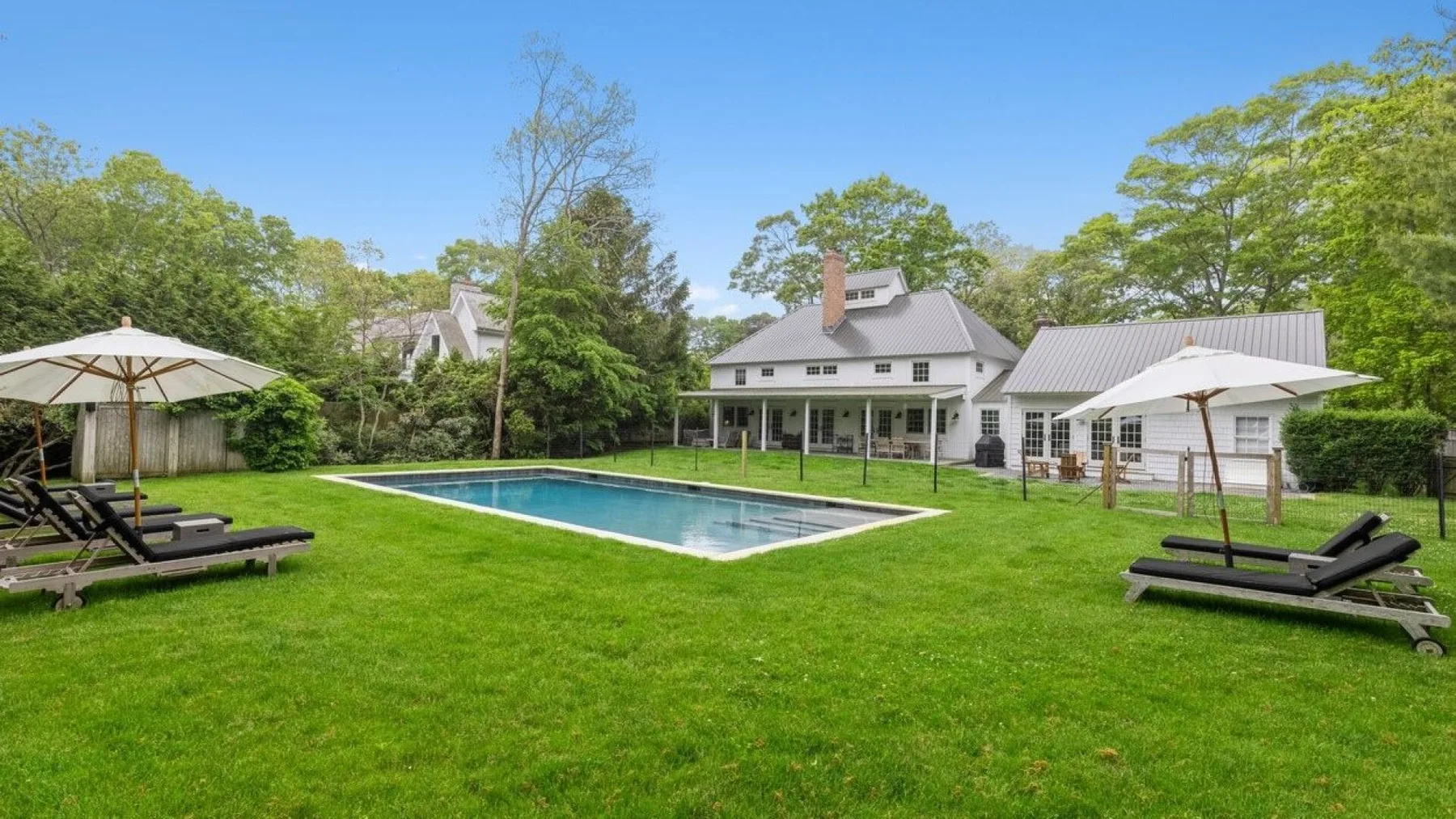 A swimming pool and lawn sit in front of a large house.