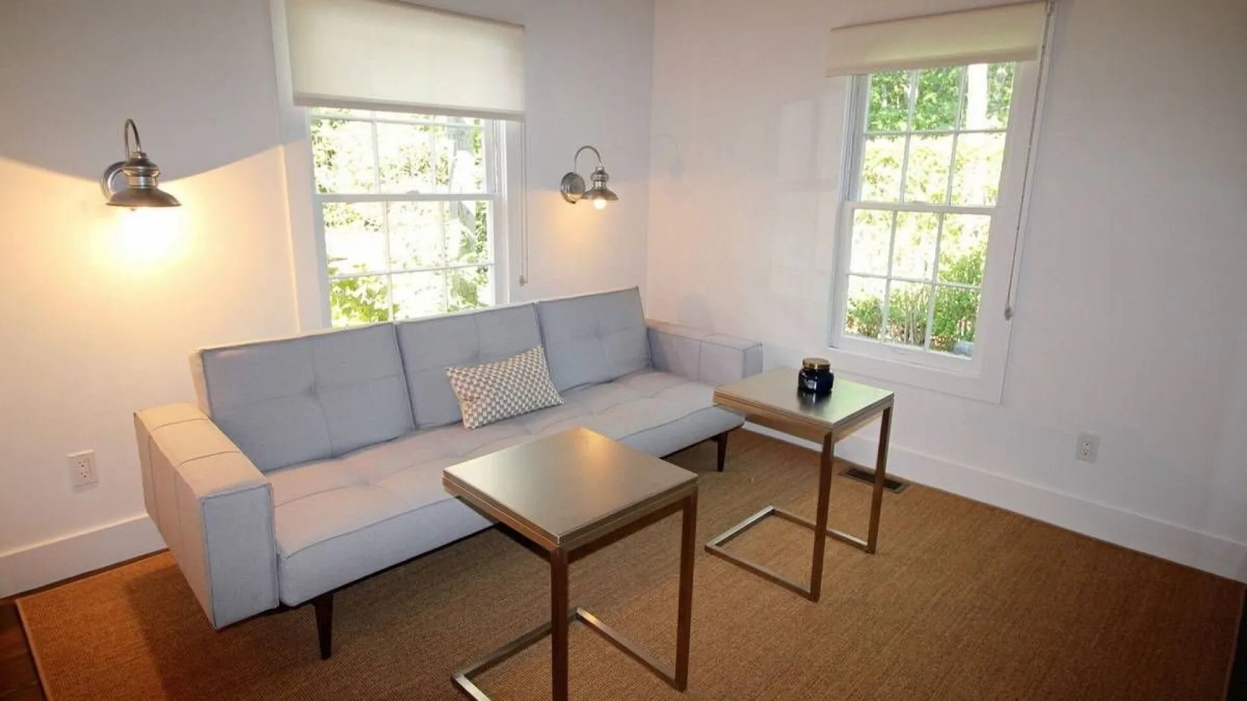 A bright living room with a gray seating area and two windows.