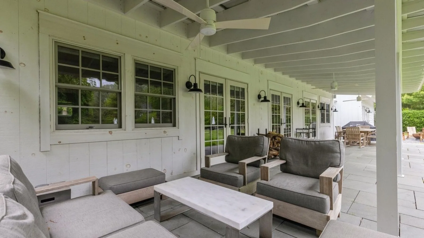 A covered porch with cushioned seating, a low table, and windows along the wall.