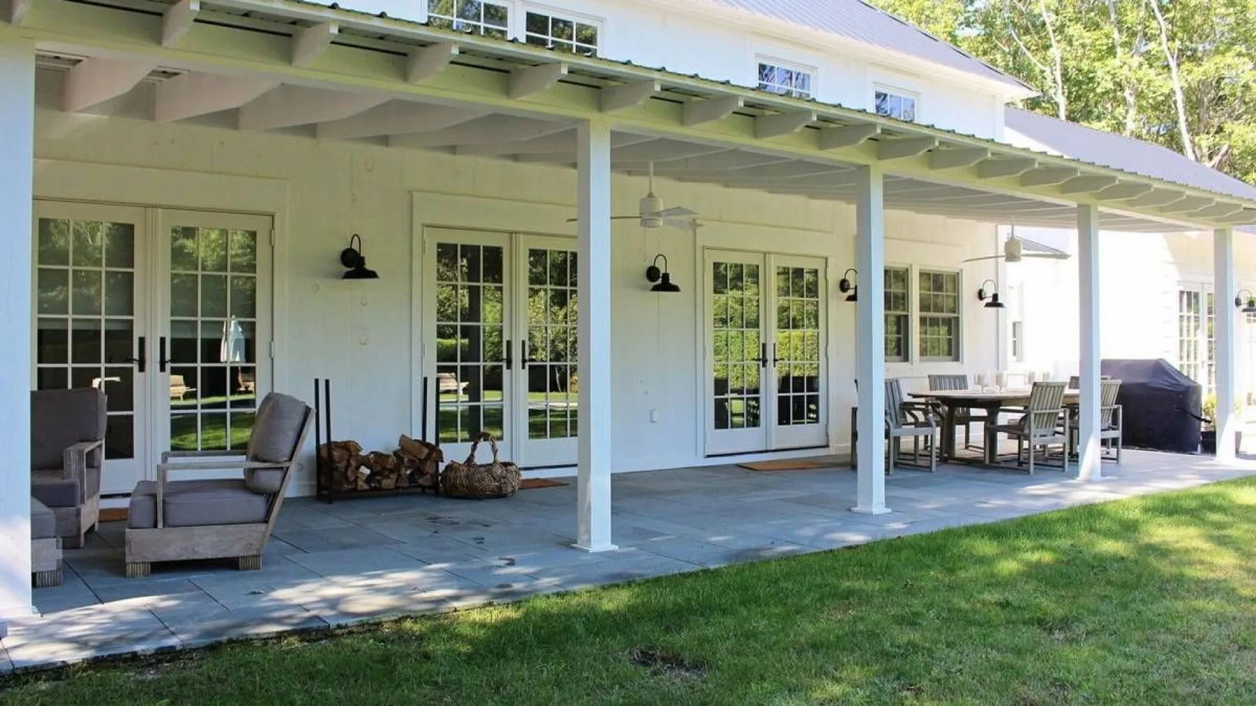 A covered patio with seating and outdoor dining furniture beside a white house.