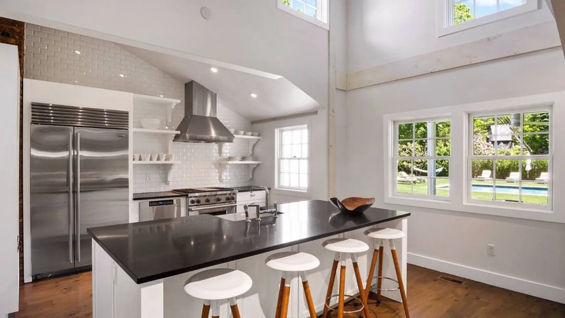 A bright kitchen with a dark island and stools beneath tall windows.
