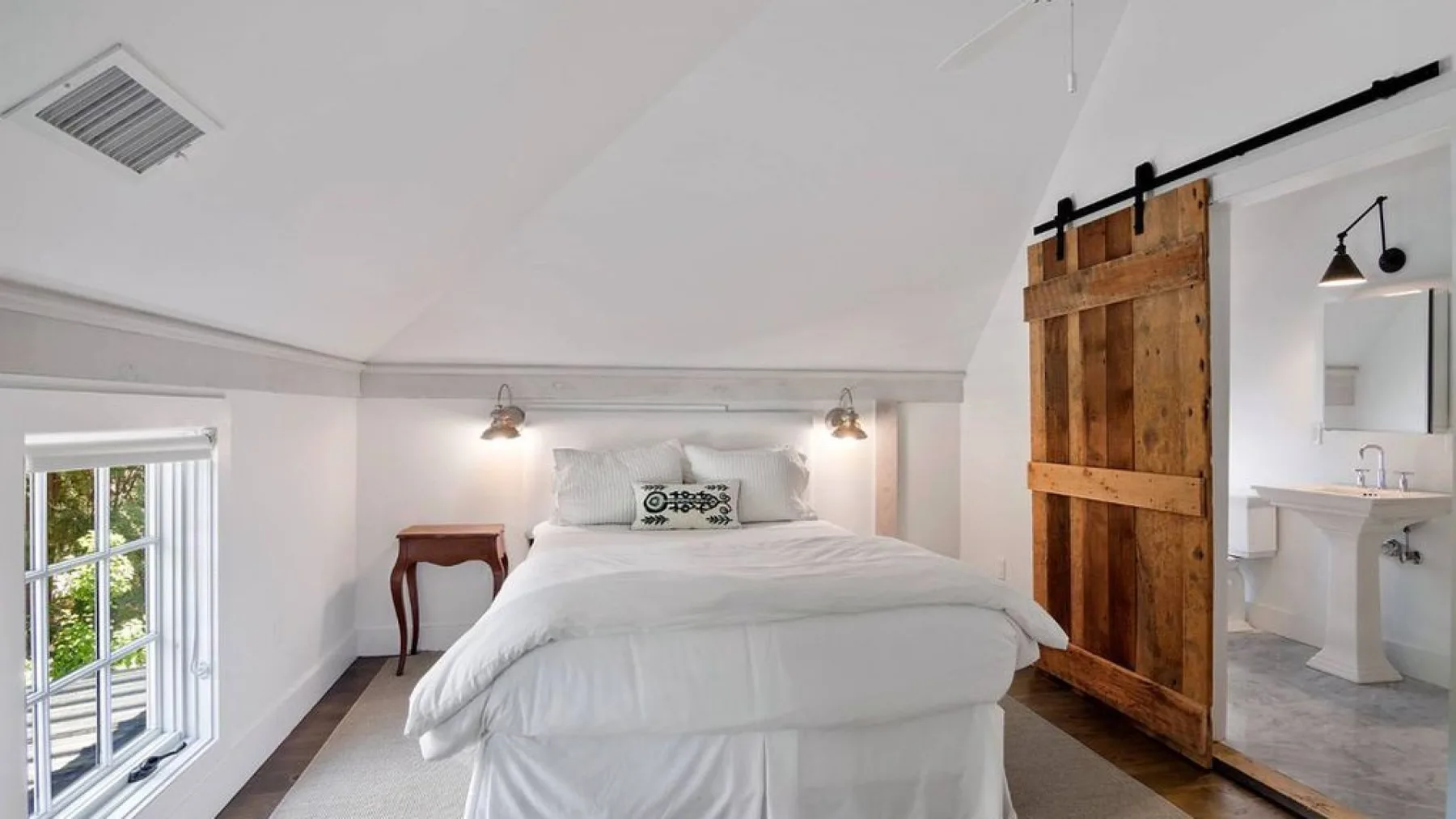 A bright bedroom features a bed beside a wooden sliding door.