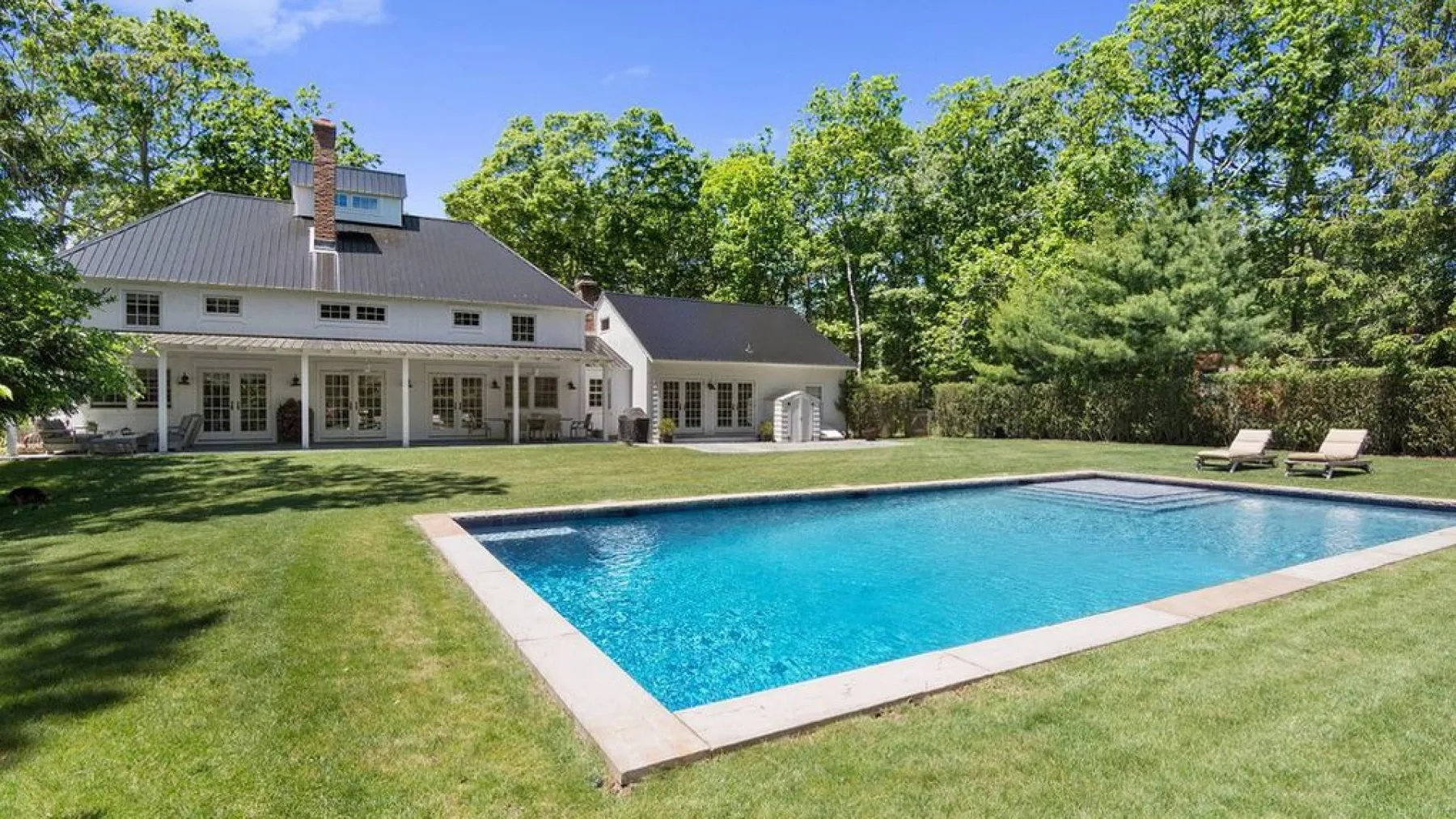 A rectangular swimming pool sits in a grassy yard beside a house.