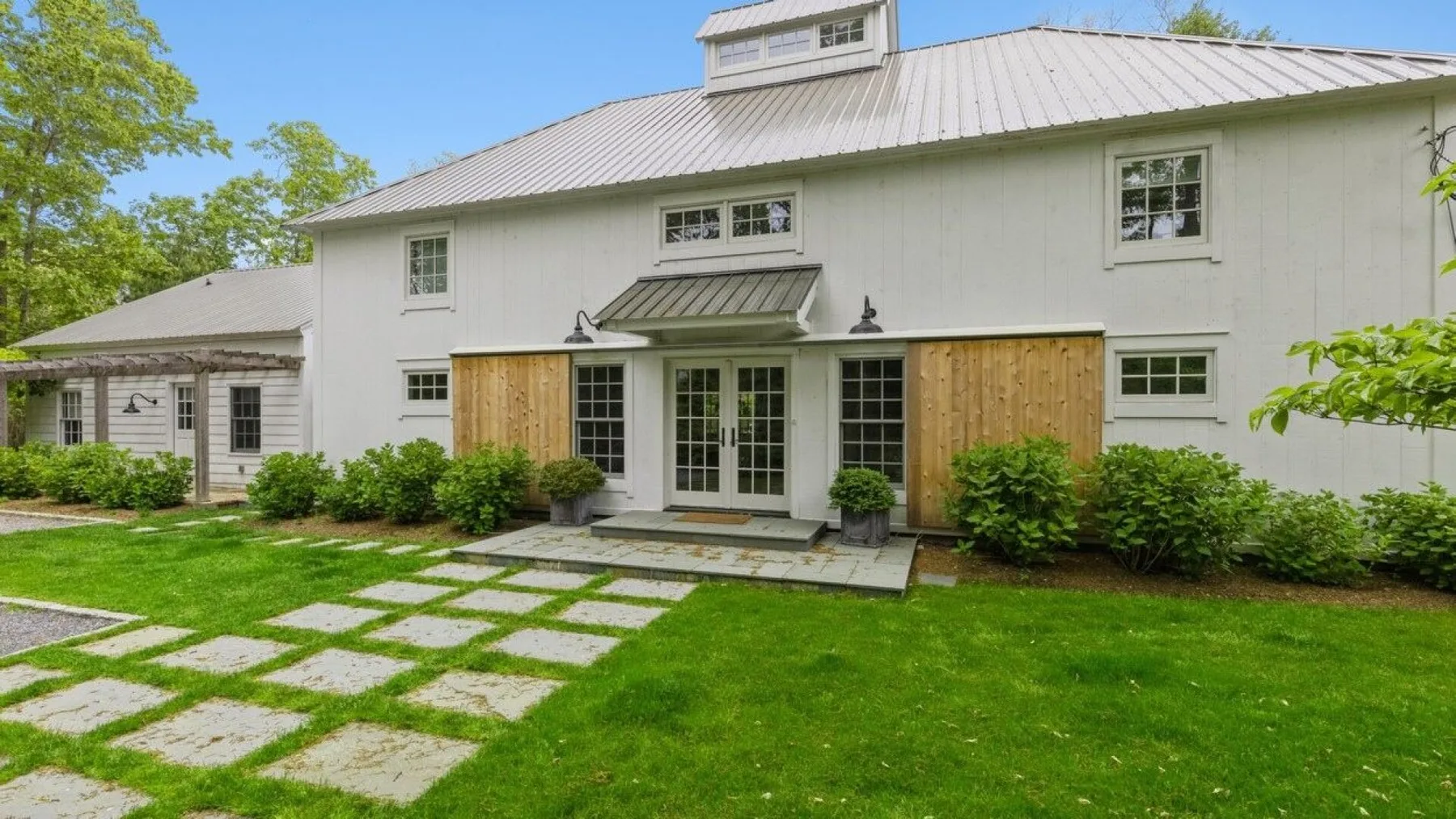 A white house with a central glass doorway, wooden panels, and a green lawn.