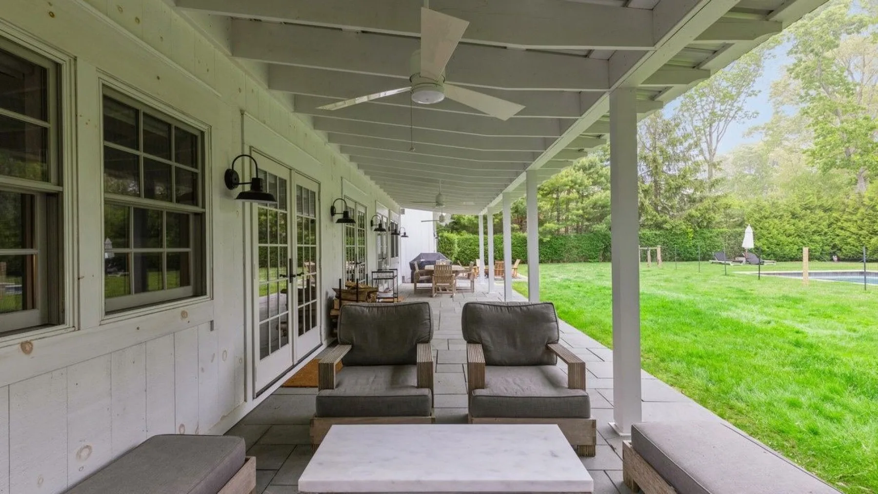 A covered outdoor patio with seating beside a green lawn.