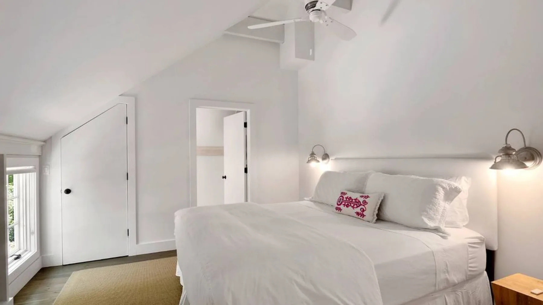 A bright bedroom features a neatly made bed beneath a sloped ceiling.