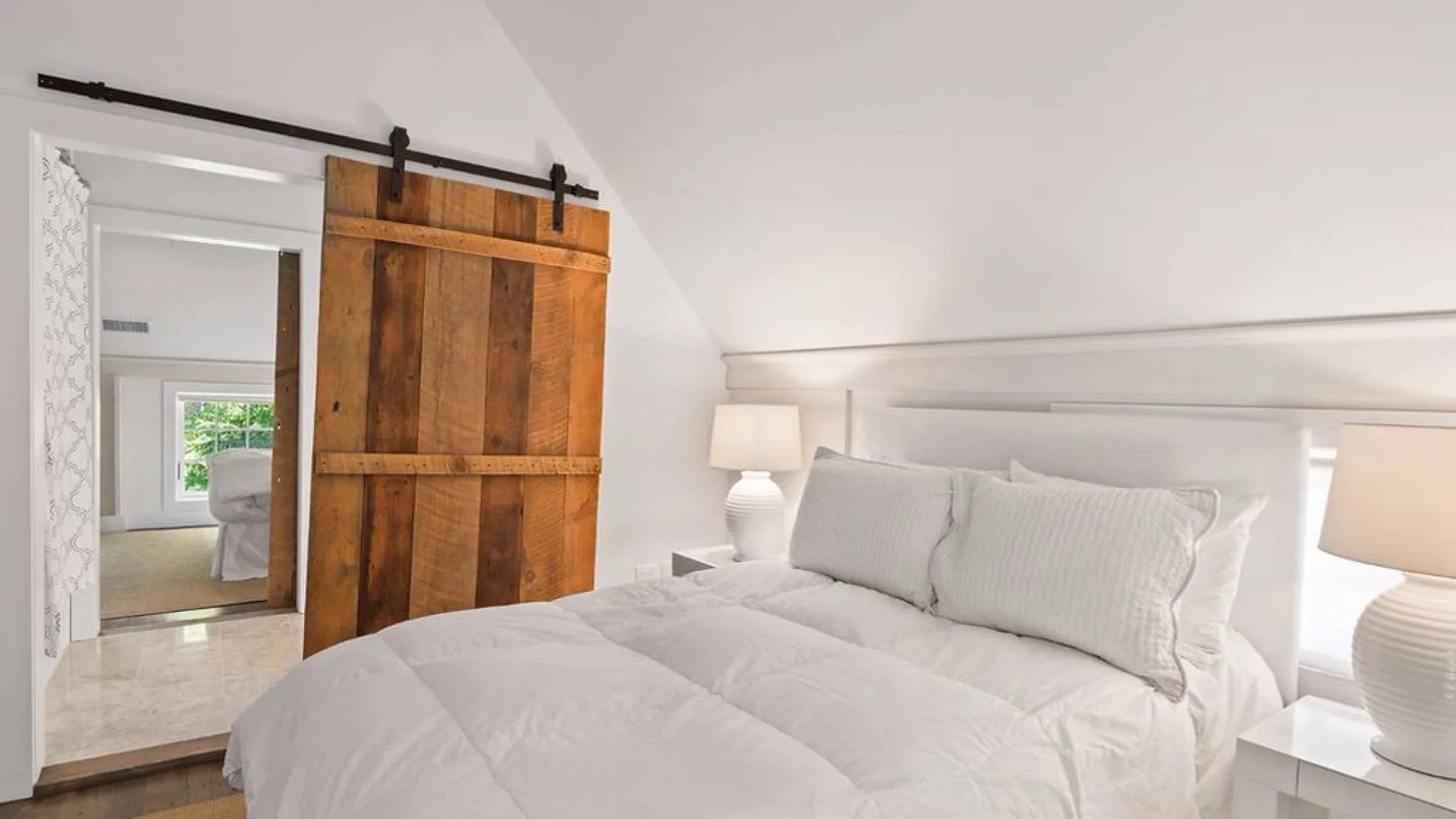 A bright bedroom with a white bed and a wooden sliding door.