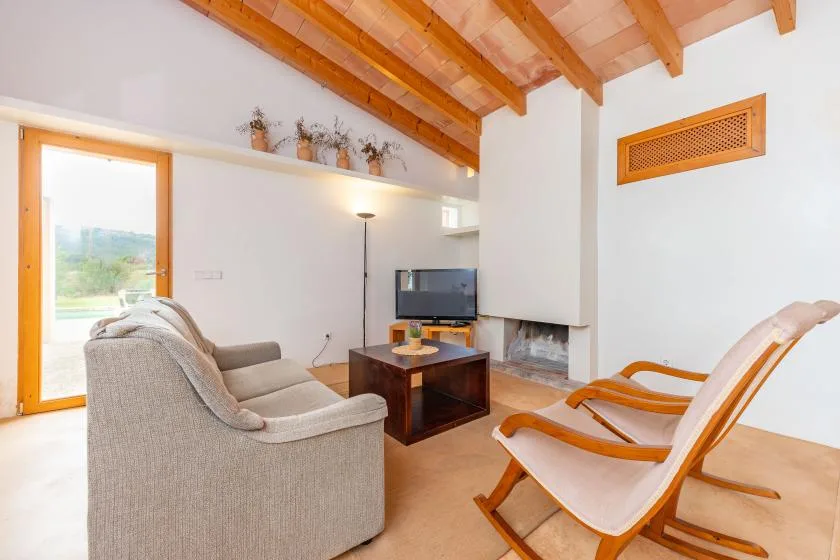 A bright living room with seating, a television, and exposed wooden ceiling beams.