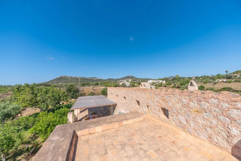 A sunlit rooftop terrace overlooks green hills and scattered buildings.